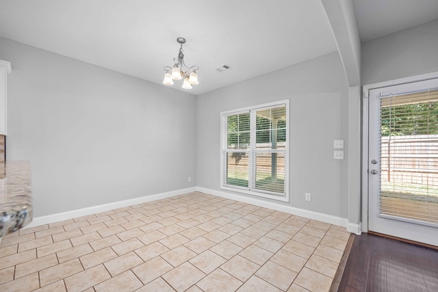 spare room featuring light hardwood / wood-style flooring, a wealth of natural light, and an inviting chandelier