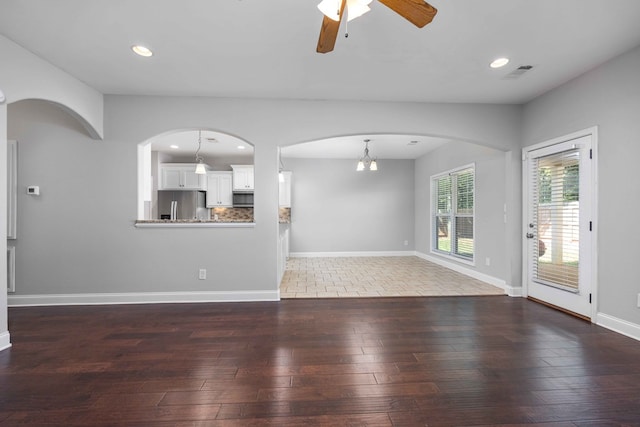 unfurnished living room featuring ceiling fan with notable chandelier and dark wood-type flooring