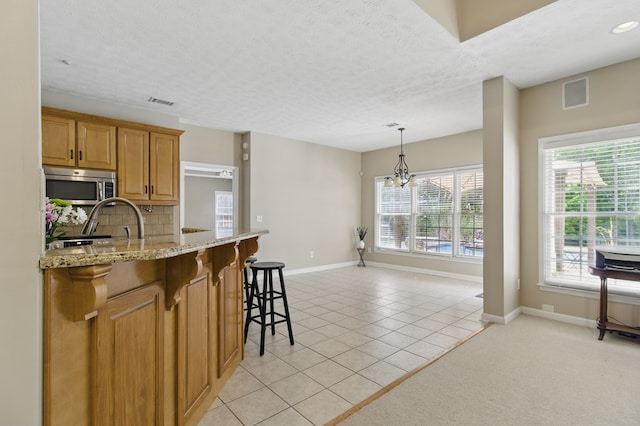 kitchen featuring stainless steel microwave, visible vents, baseboards, and light tile patterned floors