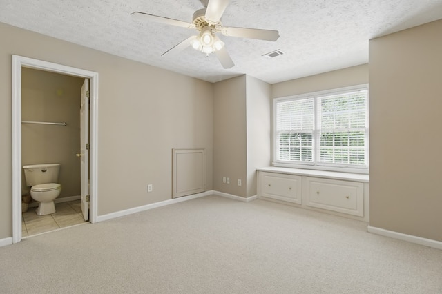 unfurnished bedroom featuring a textured ceiling, connected bathroom, light colored carpet, baseboards, and visible vents