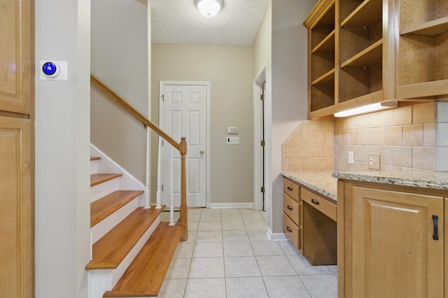 kitchen featuring tasteful backsplash, open shelves, light stone counters, light tile patterned floors, and baseboards