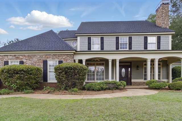 view of front of home featuring stone siding, a porch, a chimney, a shingled roof, and a front yard