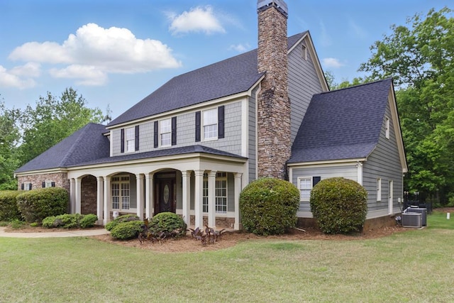 view of front facade with a porch, a chimney, roof with shingles, and a front yard