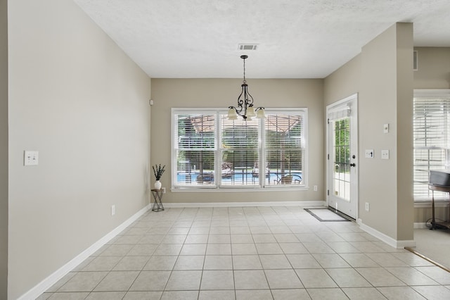 unfurnished dining area featuring baseboards, a notable chandelier, a textured ceiling, and light tile patterned floors