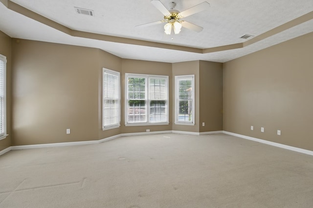 unfurnished room featuring light carpet, a tray ceiling, visible vents, and baseboards