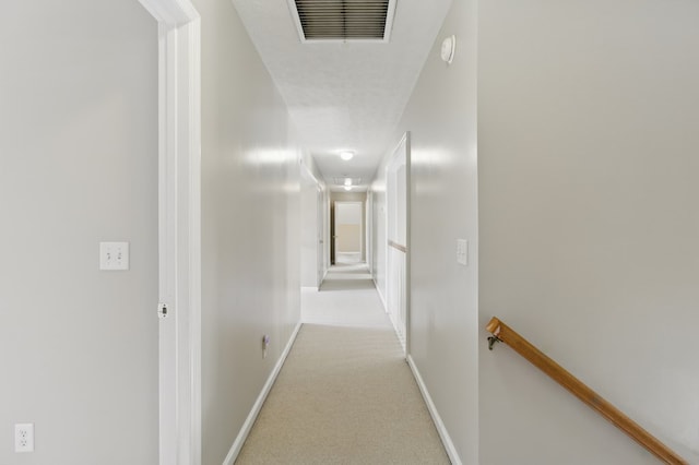 hallway featuring carpet, visible vents, baseboards, and an upstairs landing