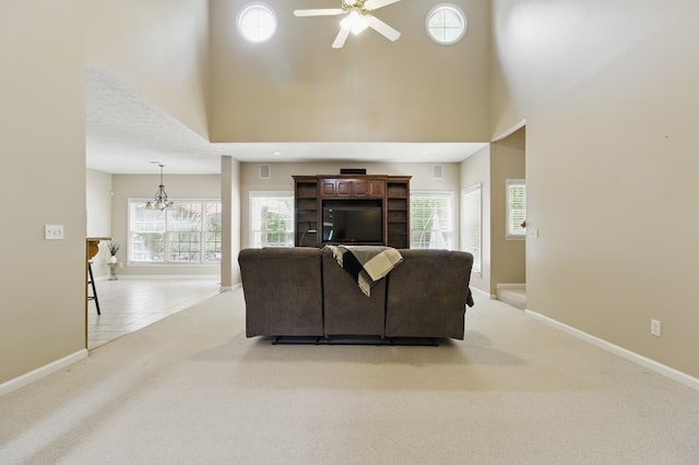 living room with a towering ceiling, baseboards, light carpet, and ceiling fan with notable chandelier