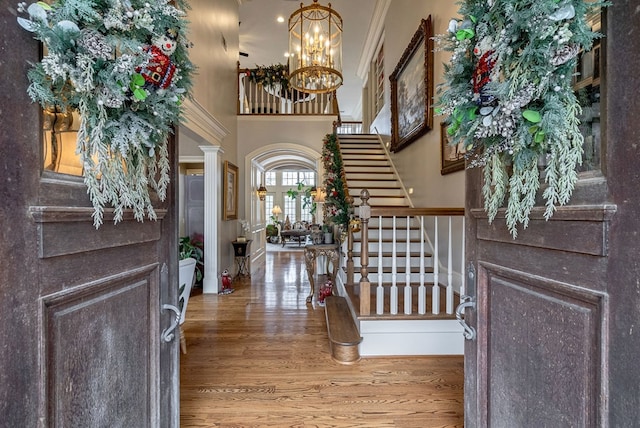 entryway featuring wood-type flooring, ornamental molding, a notable chandelier, and a high ceiling