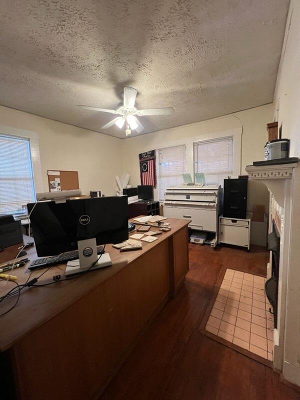 office space featuring a fireplace, ceiling fan, dark hardwood / wood-style flooring, and a textured ceiling