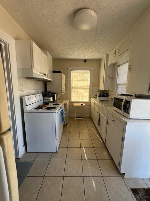 kitchen with white cabinets, light tile patterned floors, white appliances, and a textured ceiling