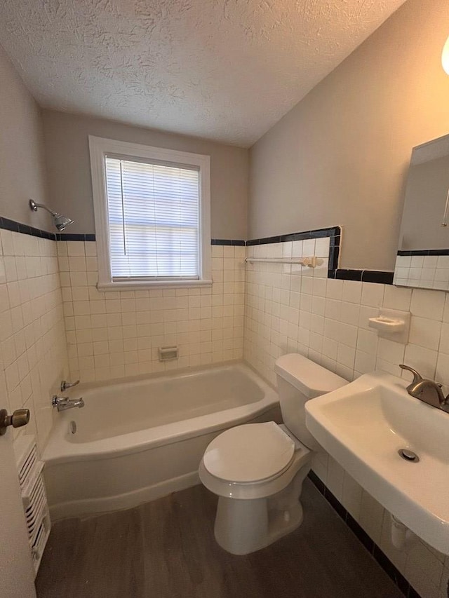 bathroom featuring toilet, wood-type flooring, tile walls, a textured ceiling, and a bath