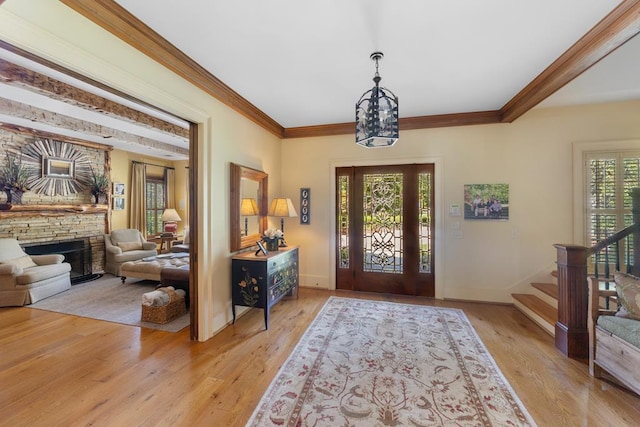 entrance foyer with light wood-type flooring, a stone fireplace, and ornamental molding