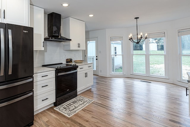 kitchen with black refrigerator, electric range oven, white cabinets, wall chimney exhaust hood, and light wood-type flooring