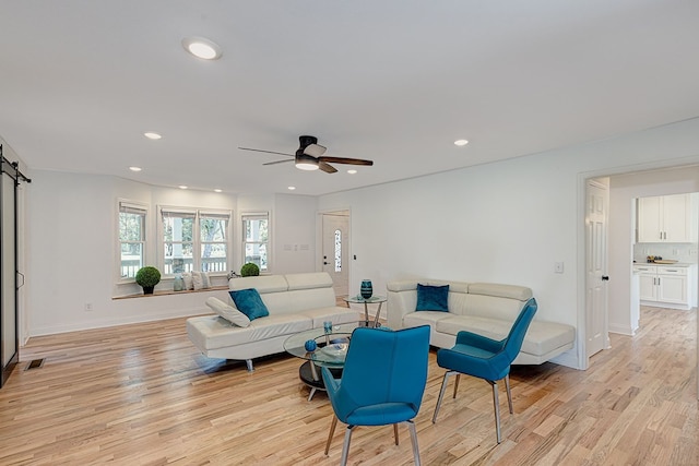 living room with light hardwood / wood-style flooring, a barn door, and ceiling fan