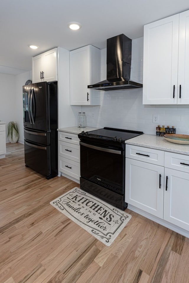 kitchen with wall chimney exhaust hood, white cabinetry, black appliances, light wood-type flooring, and backsplash