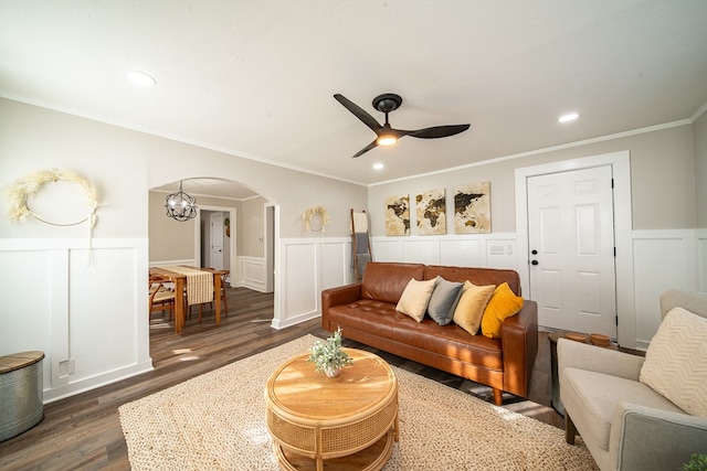 living room featuring ceiling fan with notable chandelier, dark wood-type flooring, and ornamental molding