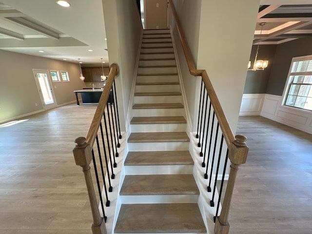 staircase featuring wood-type flooring, a notable chandelier, and beam ceiling