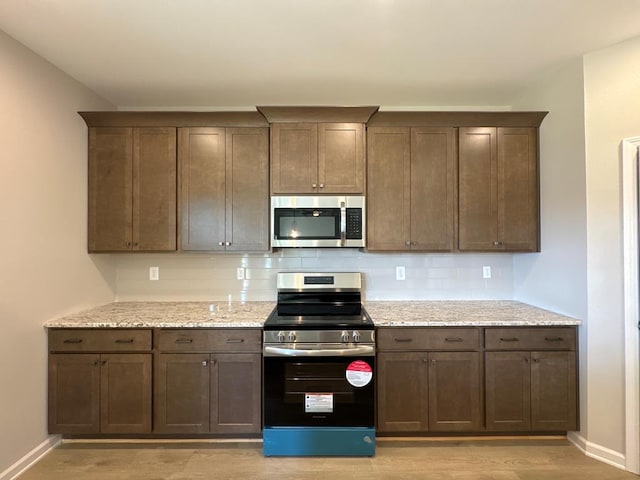 kitchen featuring light stone counters, dark brown cabinetry, backsplash, and appliances with stainless steel finishes