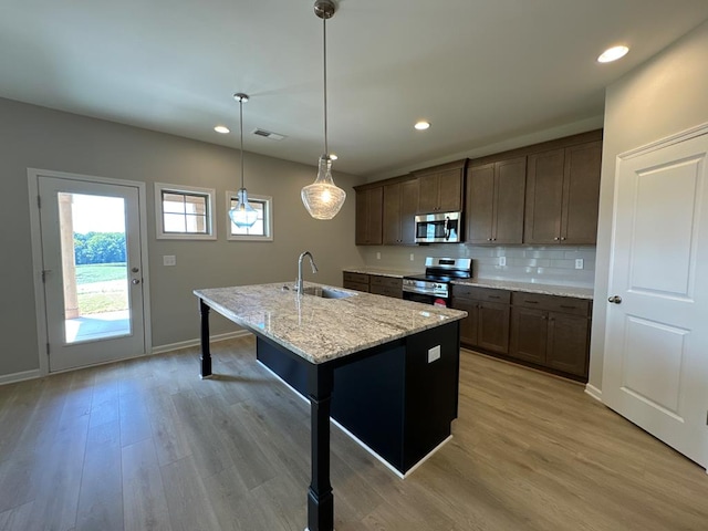 kitchen with light stone countertops, appliances with stainless steel finishes, light wood-type flooring, sink, and a center island with sink