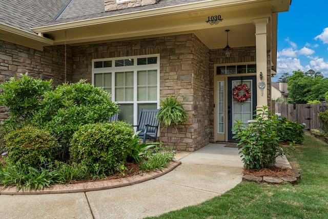 property entrance featuring stone siding, roof with shingles, fence, and covered porch