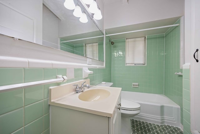 full bathroom with tile patterned flooring, tiled shower / bath, toilet, tile walls, and vanity