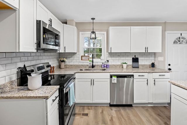 kitchen featuring white cabinets, a sink, light wood-style floors, stainless steel appliances, and backsplash