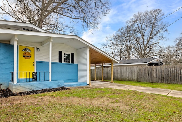 view of exterior entry featuring fence, a carport, covered porch, and brick siding