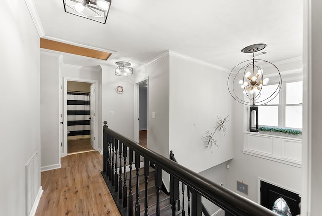 hallway with visible vents, ornamental molding, an upstairs landing, wood finished floors, and baseboards