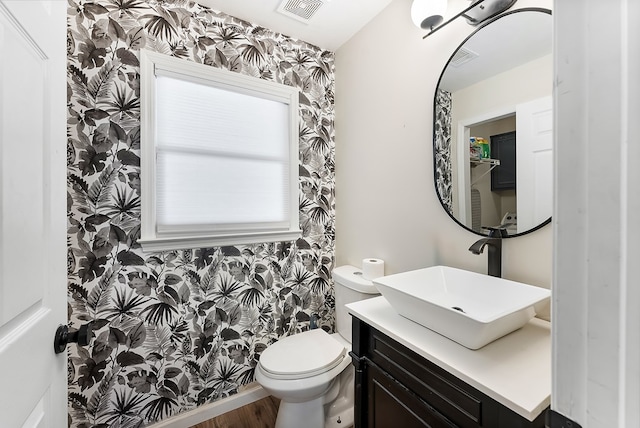 bathroom featuring visible vents, toilet, vanity, wood finished floors, and wallpapered walls