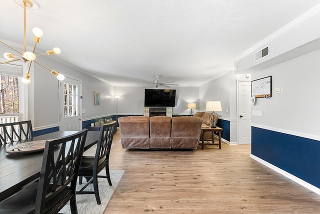 living room featuring a wainscoted wall, visible vents, ornamental molding, wood finished floors, and ceiling fan with notable chandelier