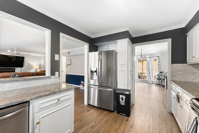 kitchen featuring appliances with stainless steel finishes, light stone counters, ornamental molding, light wood-style floors, and white cabinetry