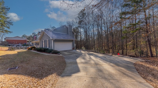 view of home's exterior featuring a garage, driveway, a chimney, and roof with shingles