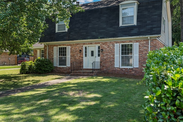 cape cod home featuring roof with shingles, brick siding, and a front yard
