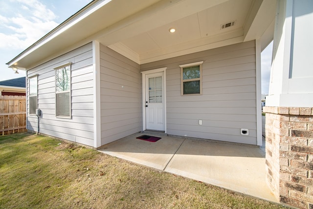 view of exterior entry with a patio, a yard, fence, and visible vents