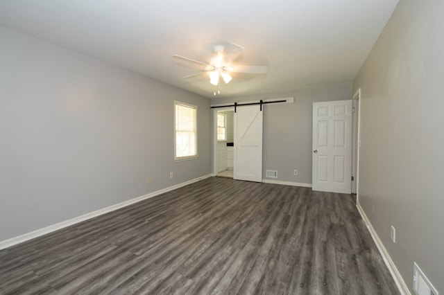 unfurnished bedroom with visible vents, baseboards, a barn door, and dark wood-style flooring