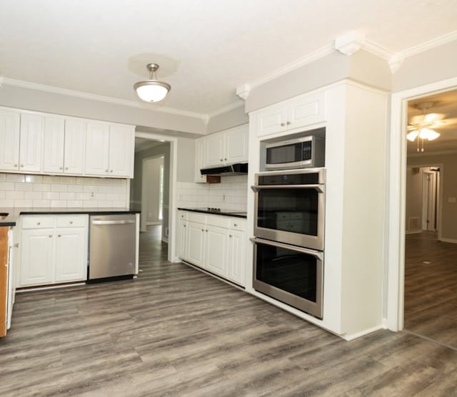 kitchen with dark countertops, ornamental molding, appliances with stainless steel finishes, wood finished floors, and white cabinetry