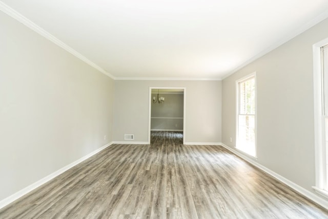 unfurnished room with visible vents, ornamental molding, wood finished floors, baseboards, and a chandelier