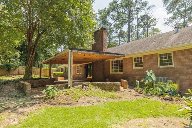 rear view of house featuring a patio, central AC, fence, brick siding, and a chimney