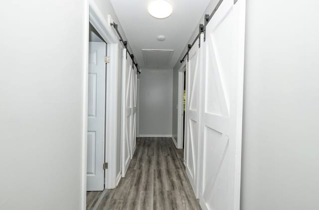 corridor featuring a barn door, baseboards, and light wood-style floors