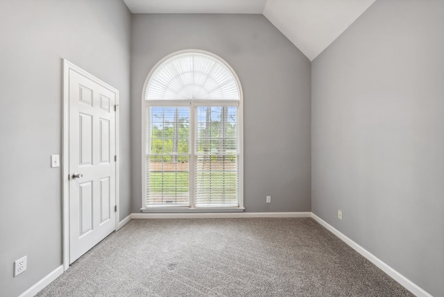 carpeted spare room with plenty of natural light, vaulted ceiling, and baseboards