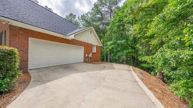 view of home's exterior with brick siding, concrete driveway, roof with shingles, and a garage