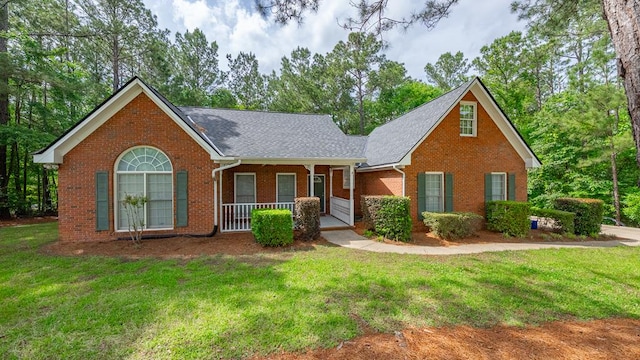 view of front of home featuring brick siding, covered porch, a front lawn, and roof with shingles
