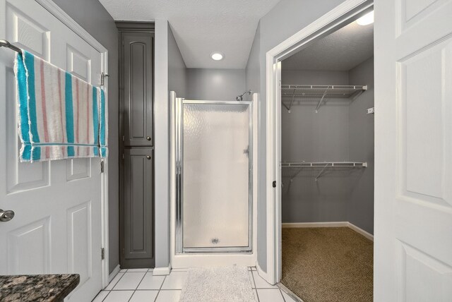 bathroom with a shower stall, a walk in closet, baseboards, tile patterned flooring, and a textured ceiling