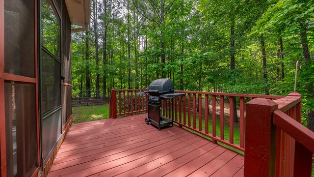 wooden terrace featuring a grill, fence, and a wooded view