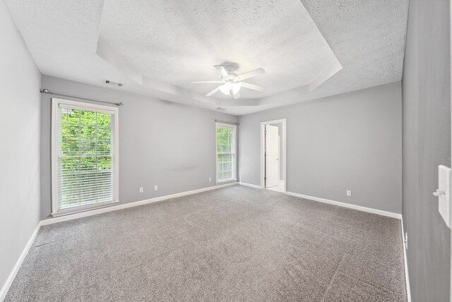 empty room featuring a textured ceiling, ceiling fan, a tray ceiling, baseboards, and carpet