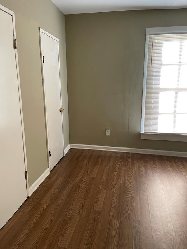 empty room featuring plenty of natural light, baseboards, and dark wood-style floors