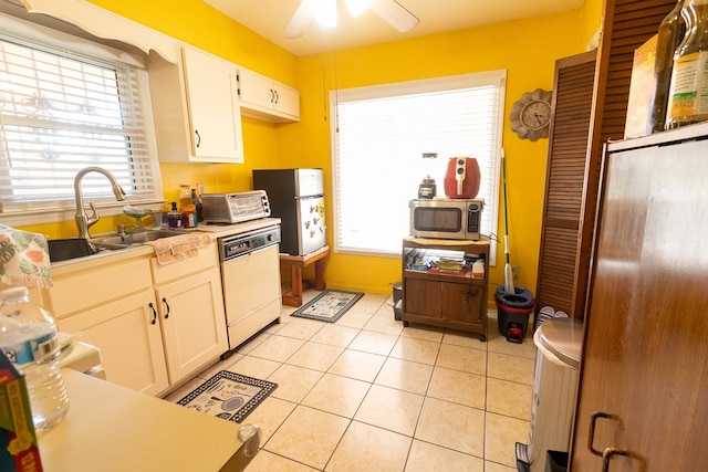 kitchen featuring light tile patterned floors, light countertops, stainless steel microwave, white dishwasher, and a sink