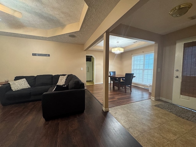 living room with a tray ceiling, a textured ceiling, dark hardwood / wood-style floors, and a notable chandelier