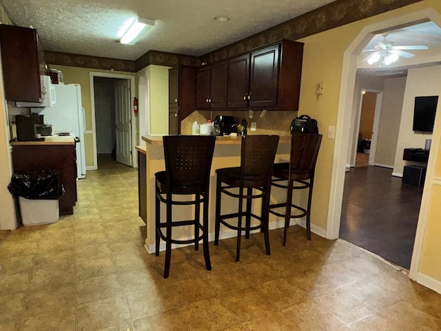 kitchen with ceiling fan, dark brown cabinetry, kitchen peninsula, and a breakfast bar area