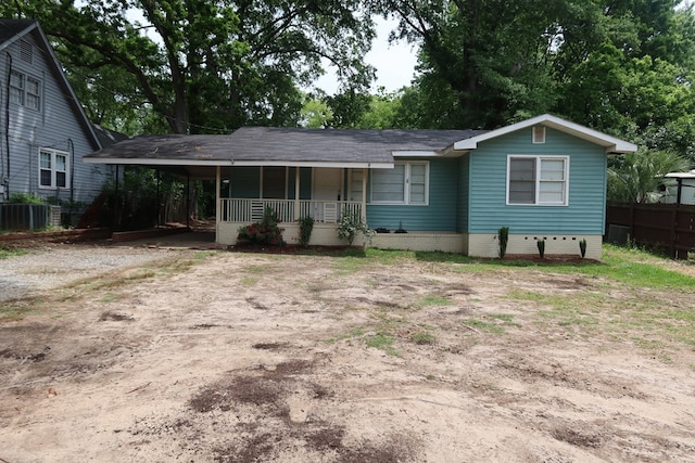 single story home featuring covered porch, dirt driveway, a carport, fence, and cooling unit